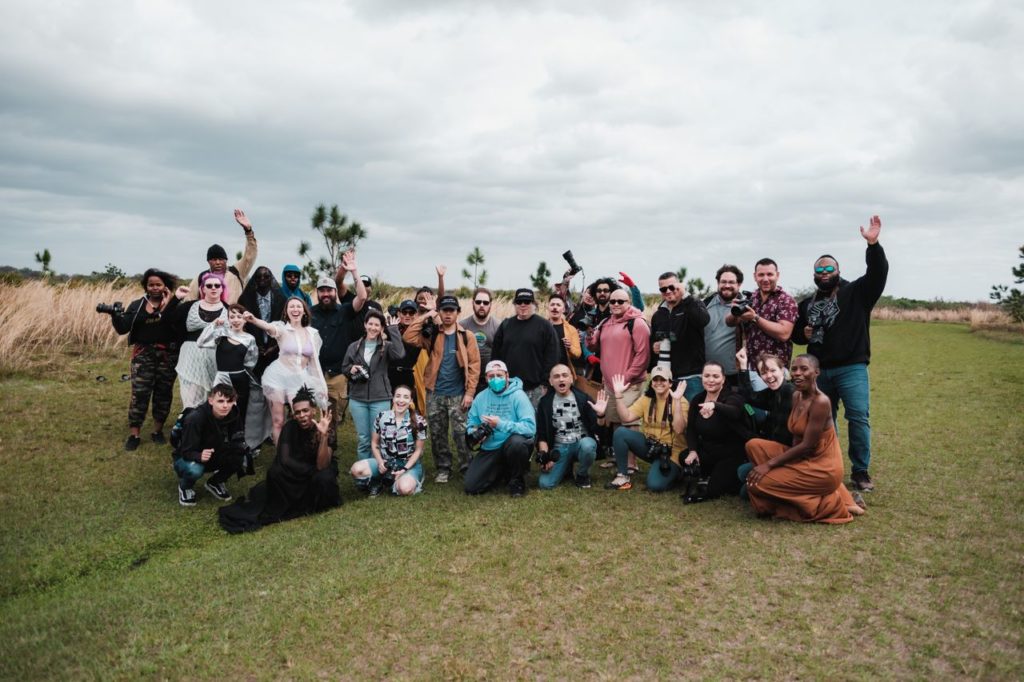 A diverse group of photographers posing together in a natural setting with cameras.
